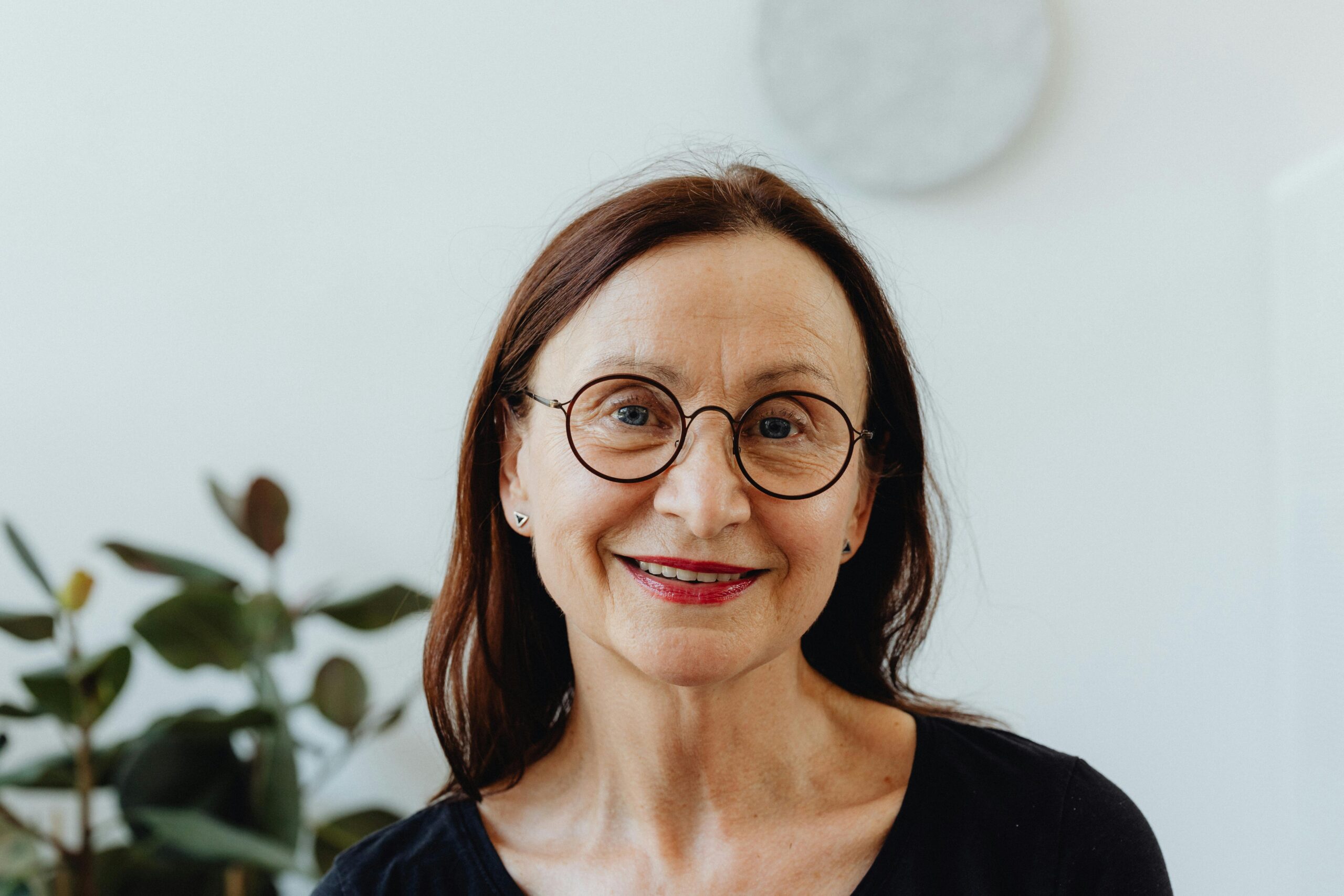 Portrait of a smiling senior woman wearing glasses against a bright indoor background.